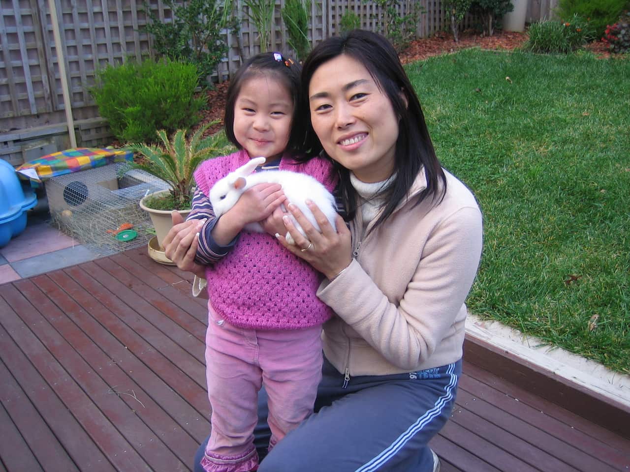 A Chinese girl holds a white rabbit and stands next to her mother. 