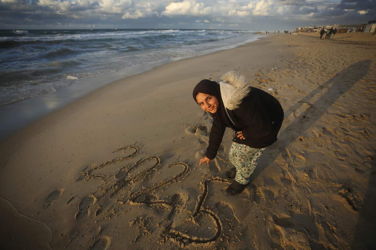 A woman draws '2025' in the sand at a beach.