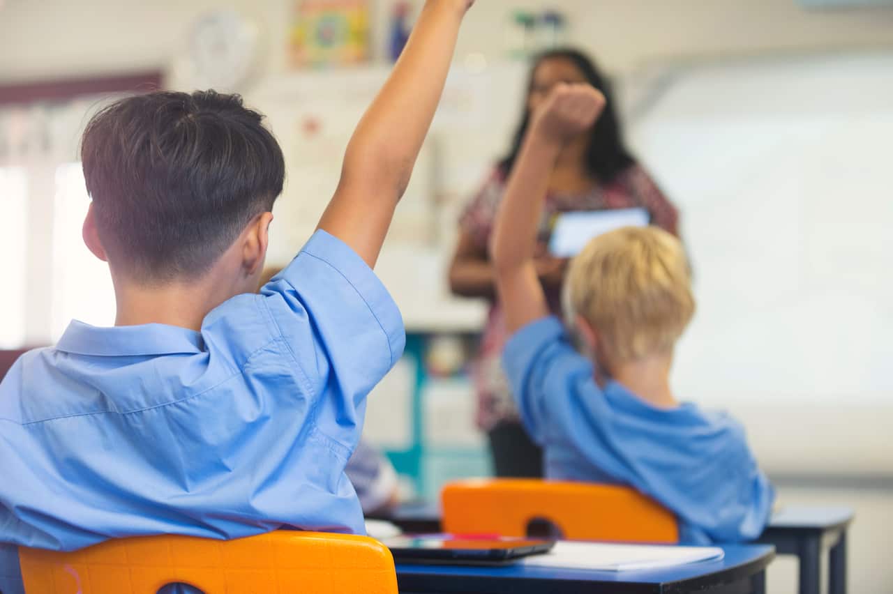 Two students in a classroom putting up their hand.