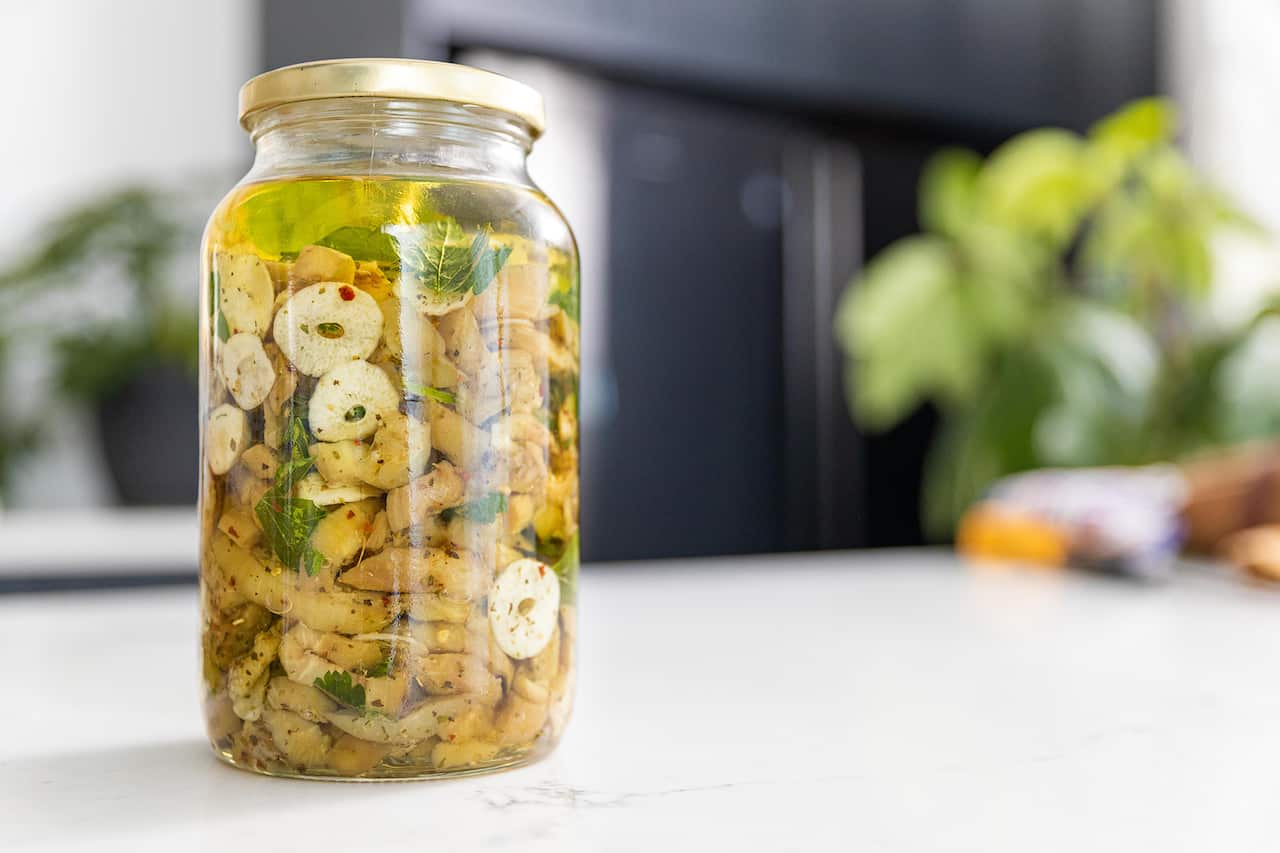 A glass jhar holds pieces of eggplant and slices of garlic in a golden liquid.