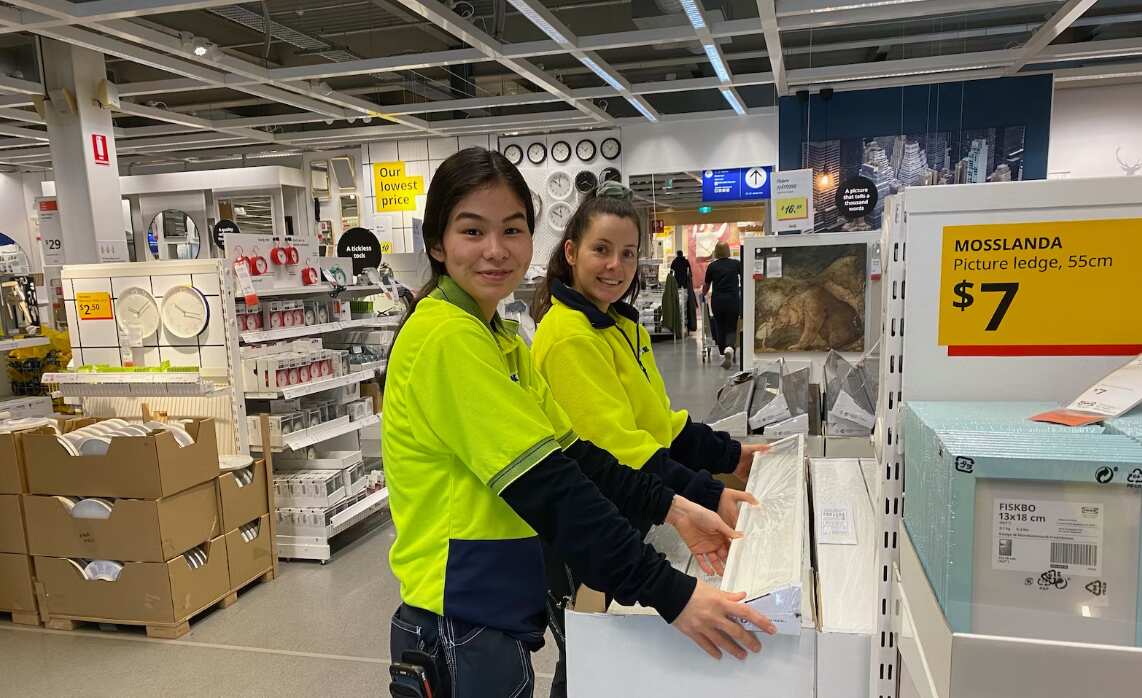 Zeynab Noori helps to place products on the shop floor. She stands next to a female co-worker.