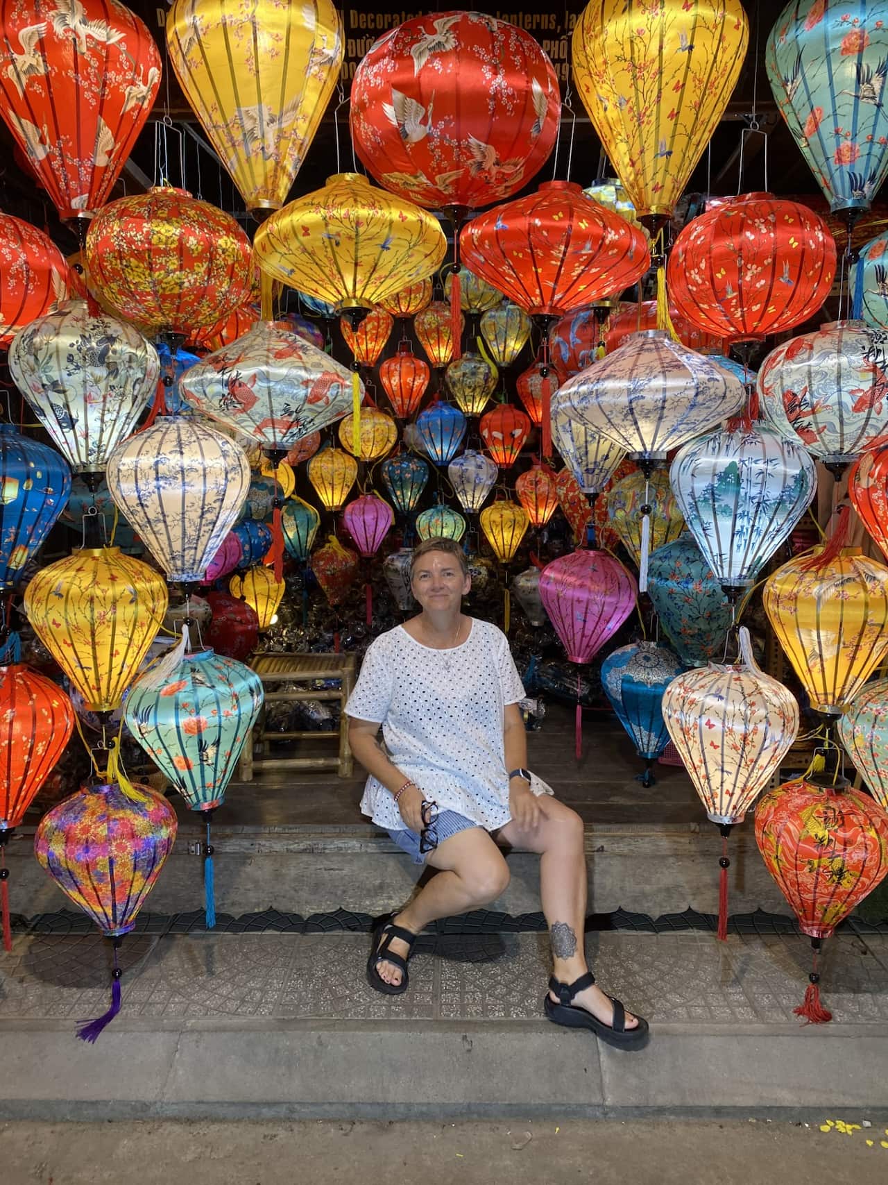 A woman sits on some stone steps and smiles, surrounded by colourful lanterns.