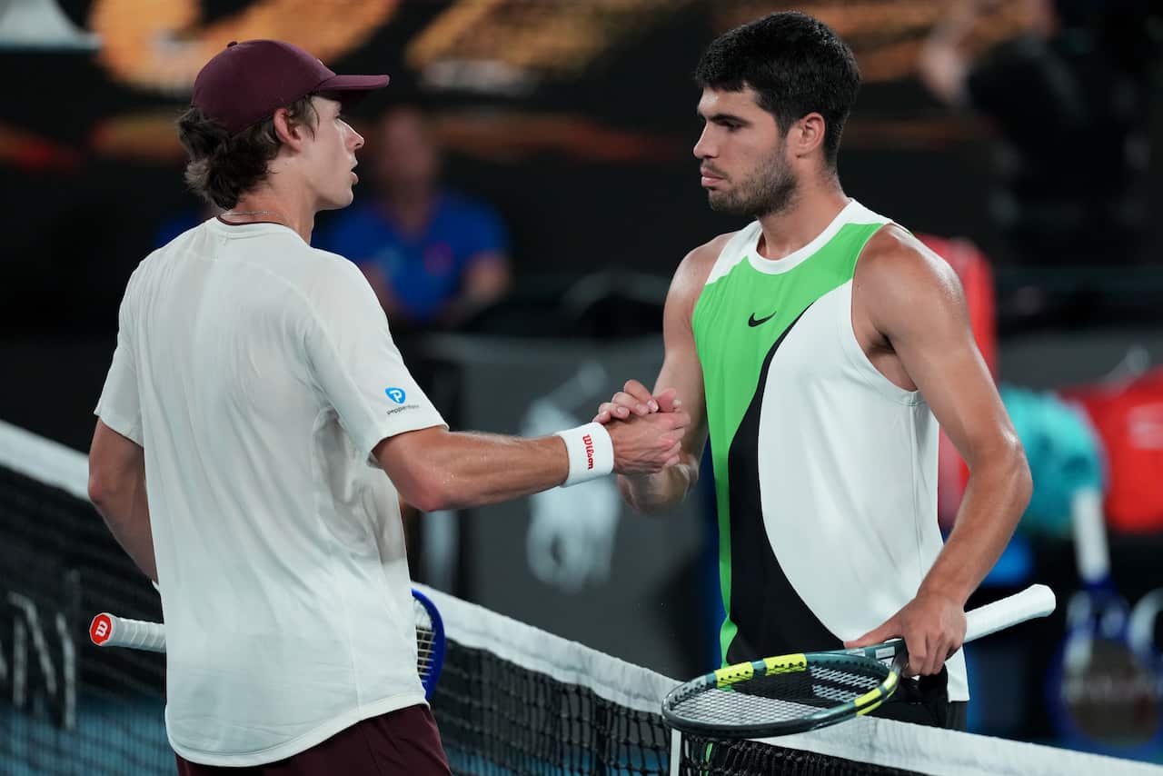 Two male tennis players shaking hands over a net, both holding raquets