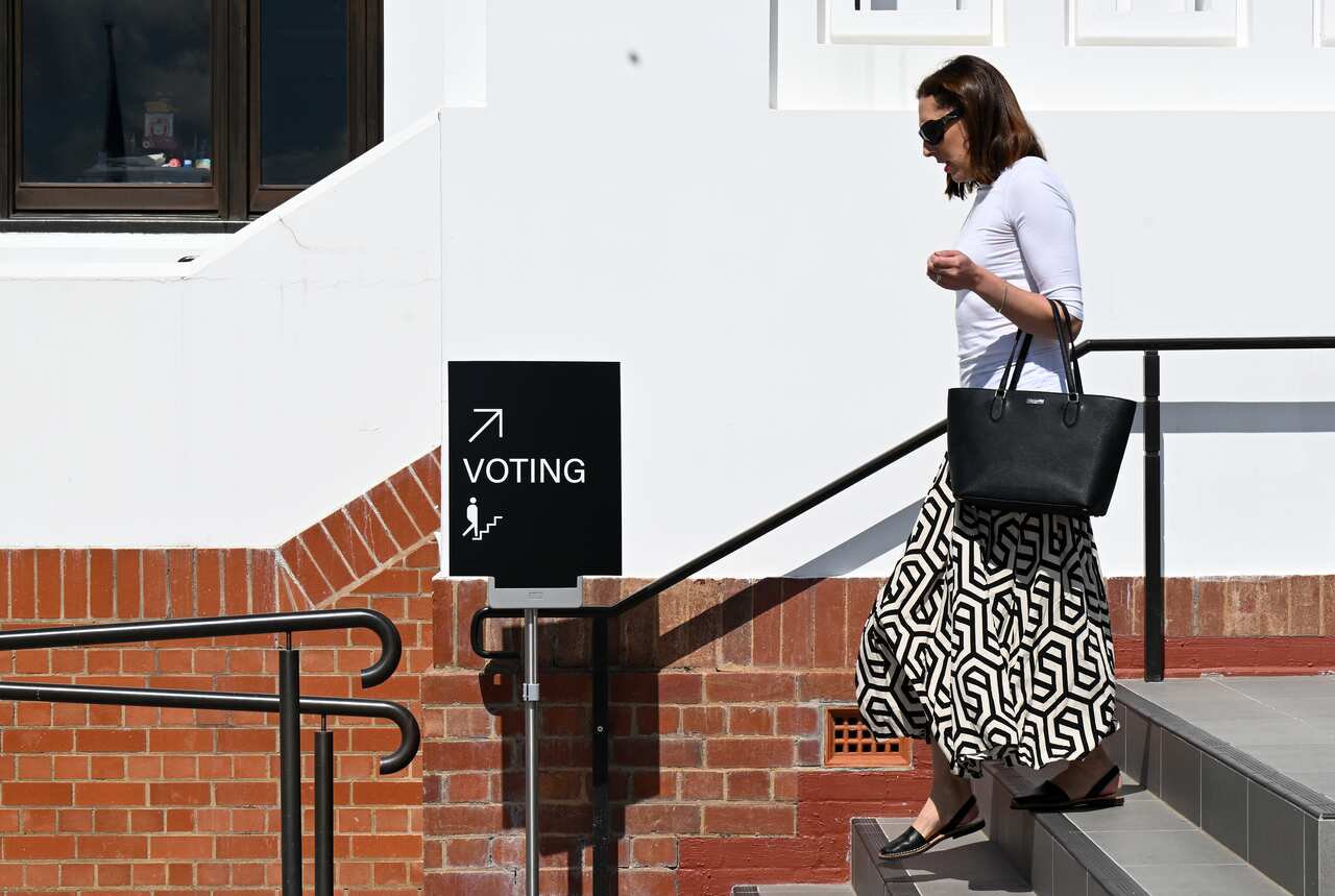 A woman wearing a black and white patterned skirt walks down the stairs near a sign directing people to a polling booth.