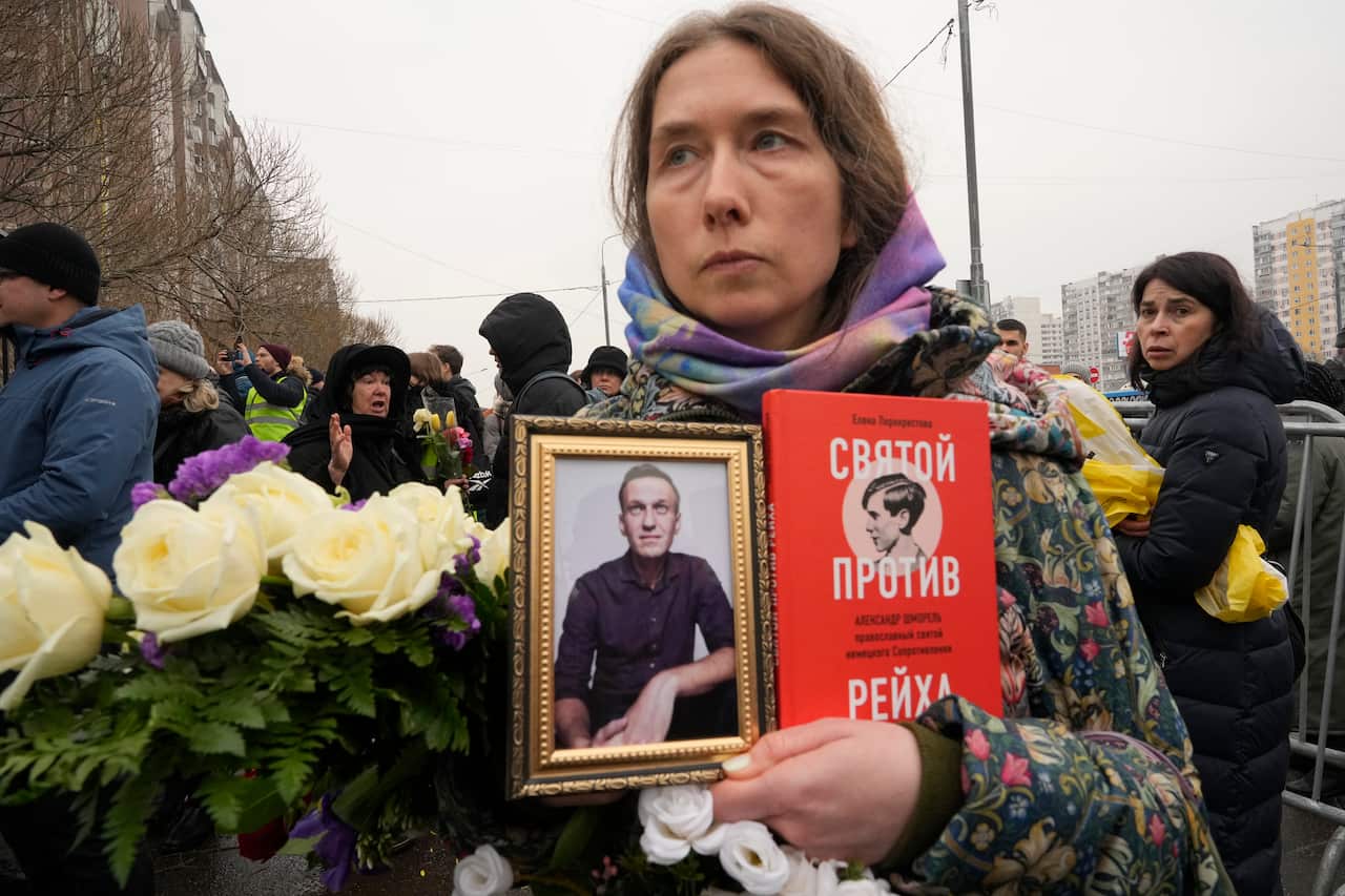A woman holds a book and a photo of Alexei Navalny
