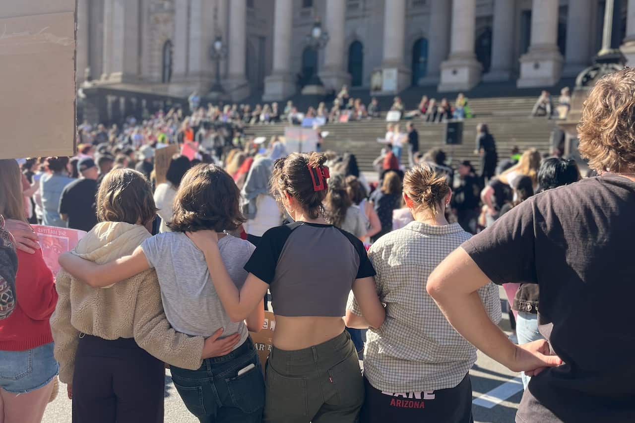 A crowd of people is gathered at a protest, holding signs and banners with various messages.