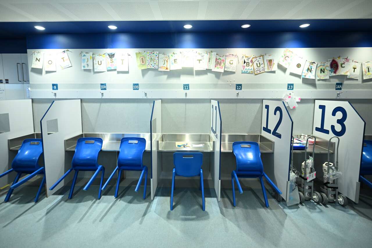 Rear view of a room with a long metal desk separated by dividers. There are blue chairs at the desk.