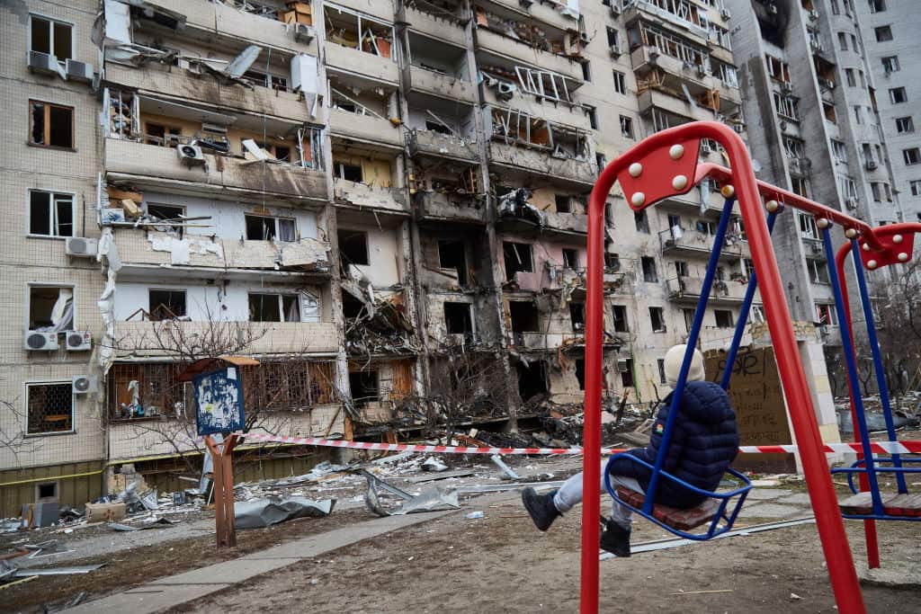 Apartment building in Ukraine destroyed. A person in a playground swing looks at the damage