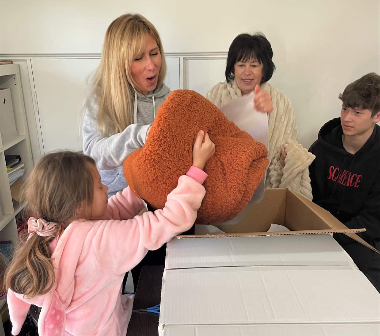 Alla Storozhuk and a young girl take blankets out of a box. There is a woman standing to Alla's left and a young boy next to the woman.