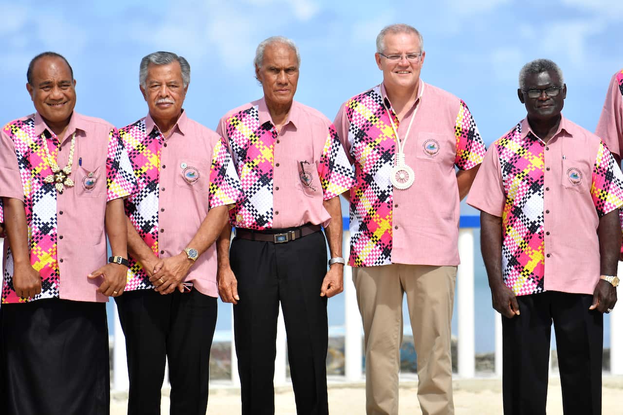 Five men in pink patterned shirts standing in a row outside