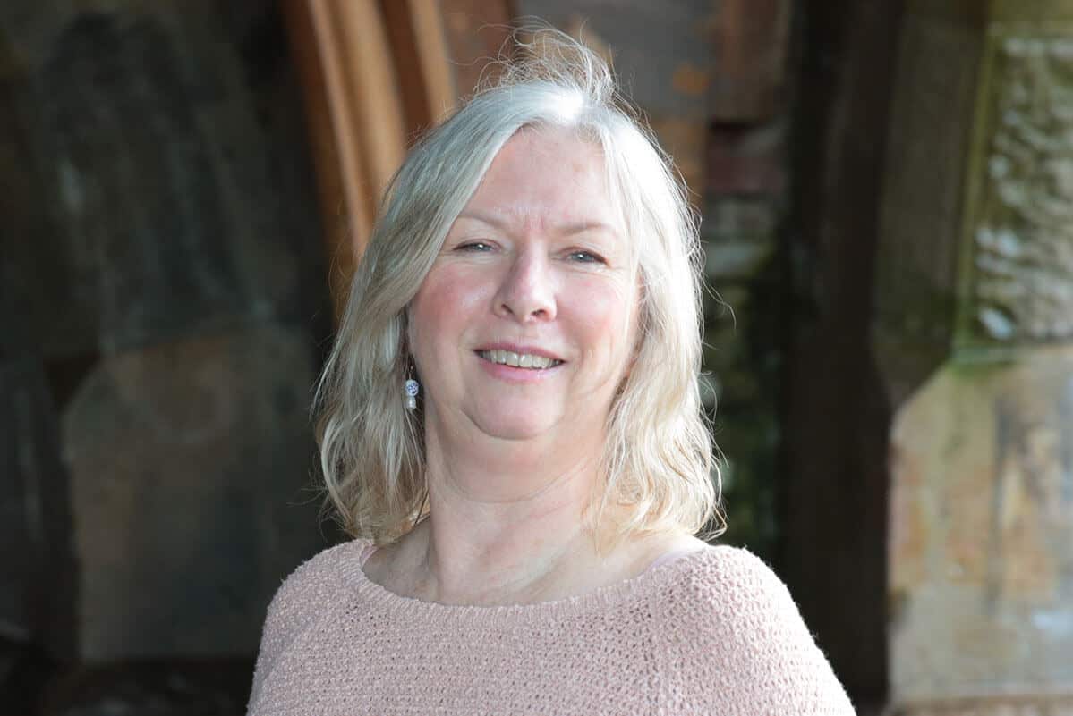 A blonde woman in a light pink jumper smiling at the camera.