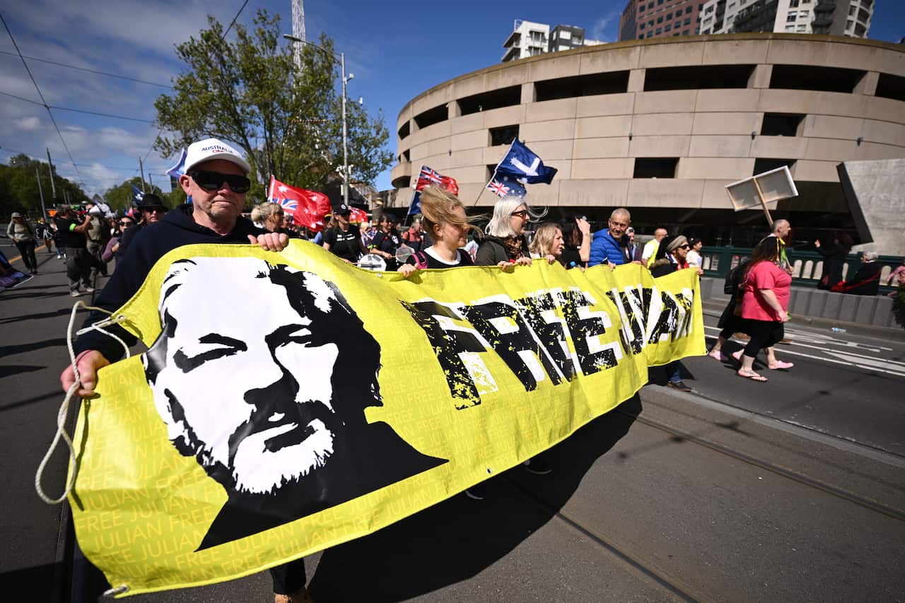 Demonstrators holding a banner that reads "FREE JULIAN" while others walk behind them.
