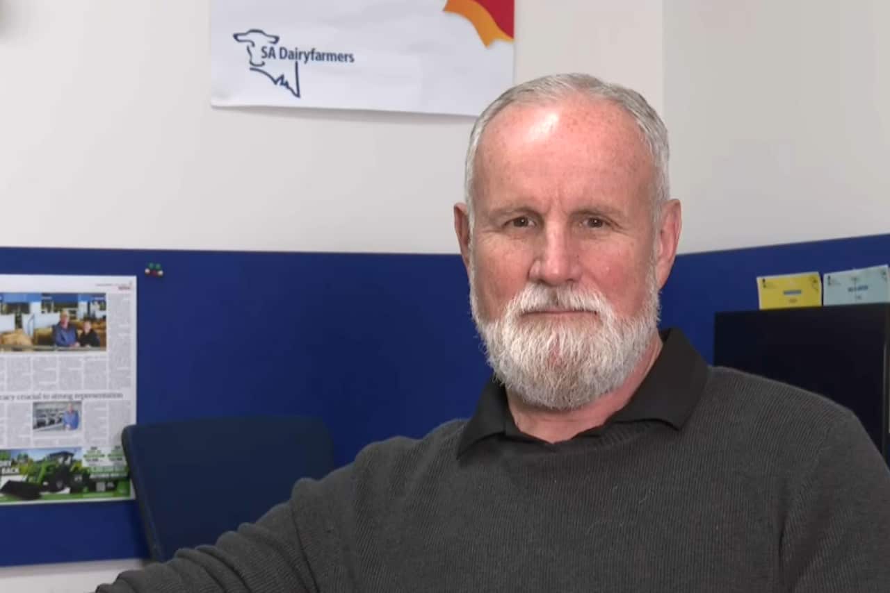 John Elferink, wearing a grey jumper, sitting in front of a blue cubicle and white wall.