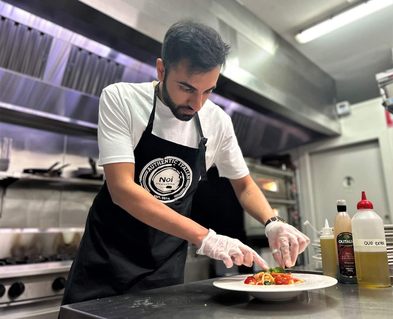 Chef stands over a plate of food at a restaurant bench.