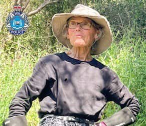 A woman wearing a wide-brimmed hat and grey long-sleeve shirt in front of bushland.