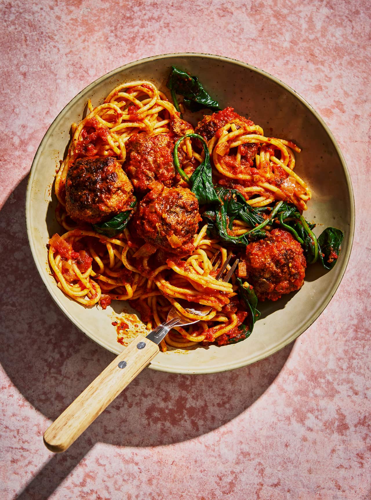 Spaghetti, meatballs and greens sit in a pottery bowl.