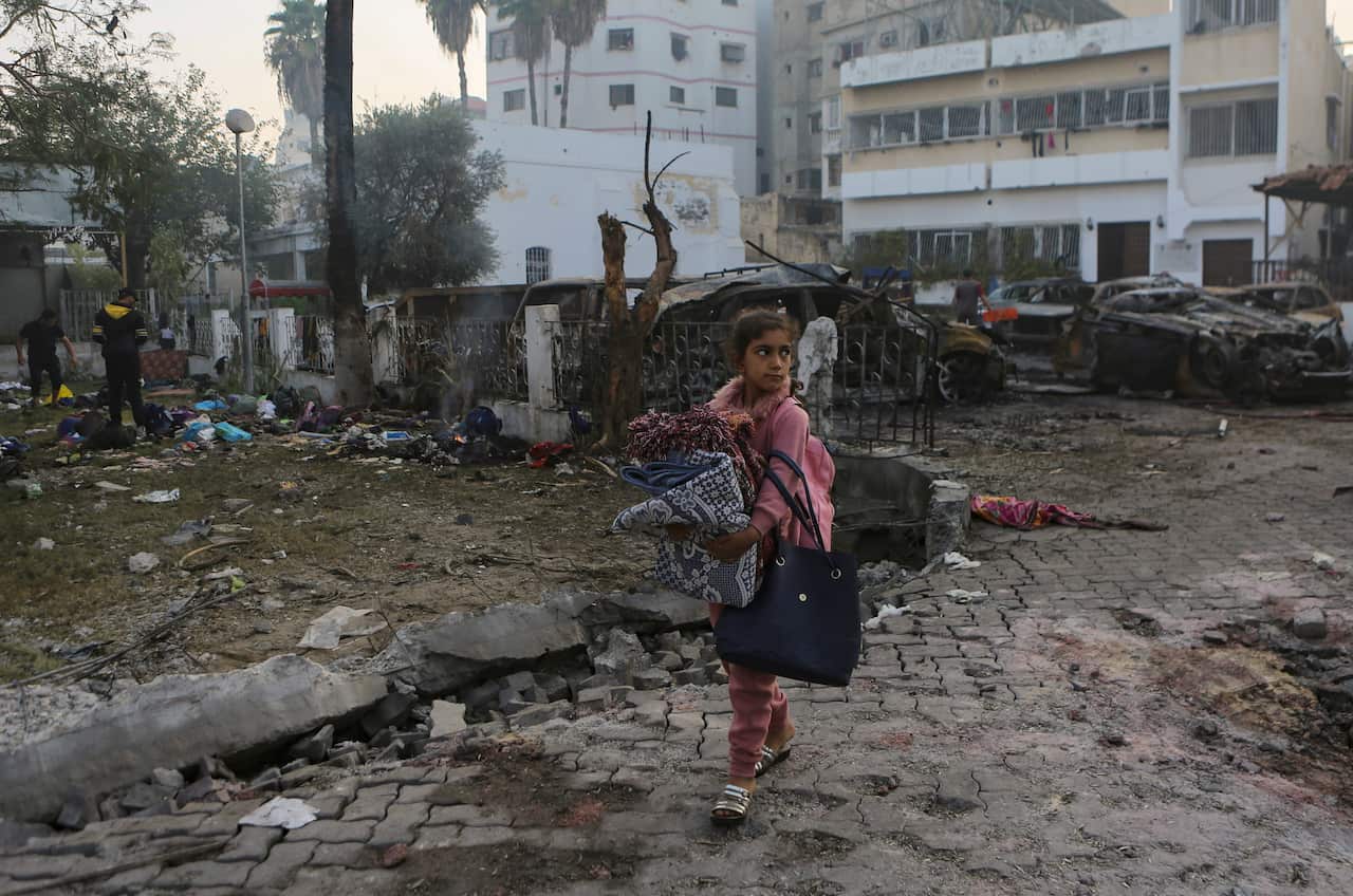 A young girl carrying blankets walking past a bomb site.