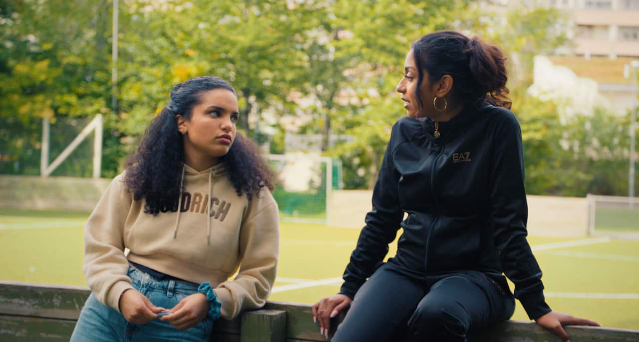 Two teenage girls lean on a fence, talking. 