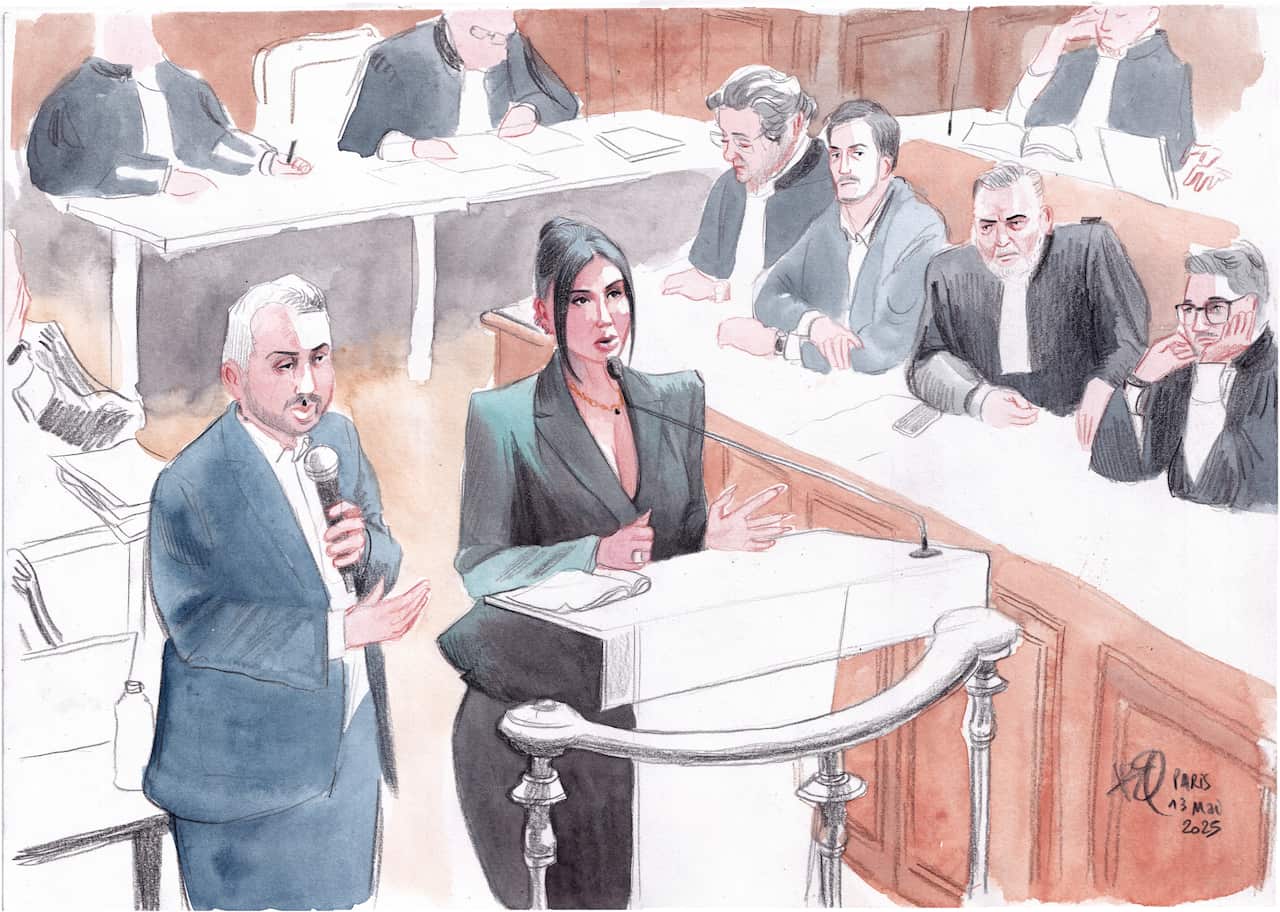 A court sketch shows a woman in a black dress testifying on the stand, with a man in a black suit standing next to her, speaking into a microphone. People in black suits are sitting in rows on tables around them.