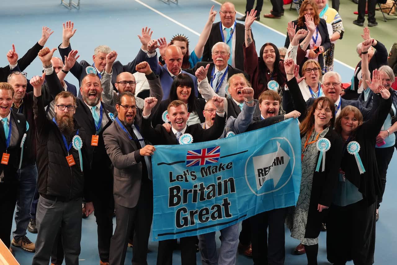 Reform UK supporters celebrate while holding a "Let’s Make Britain Great" banner at an election event.