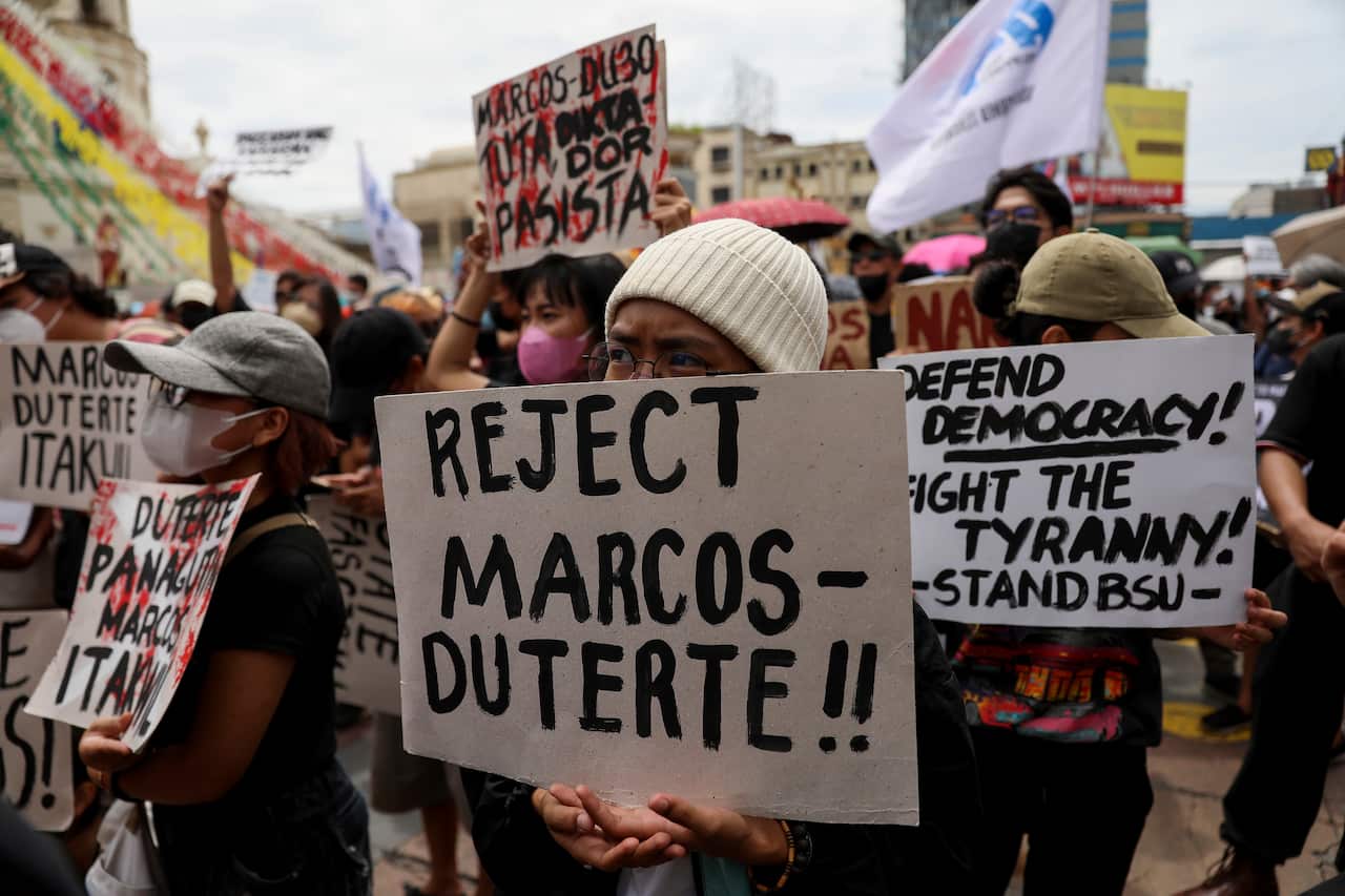 A crowd of people holding signs. One reads "Reject Marcos-Duterte" while another says "Defend Democracy".
