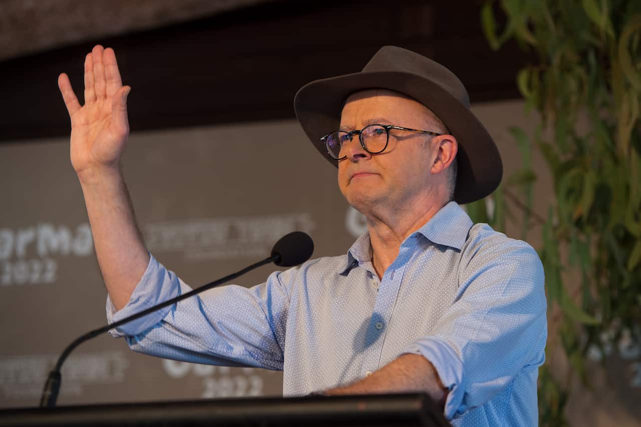 Anthony Albanese, wearing a button-down shirt and akubra, at a podium. He is waving his hand.