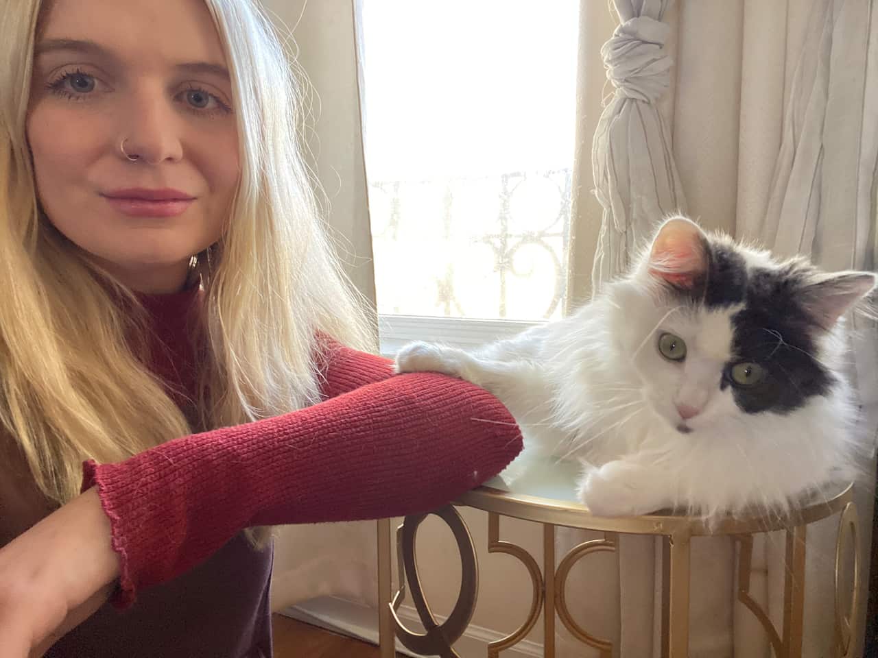 Woman with blonde hair sits near a white and black cat, that has its paw on her arm. 