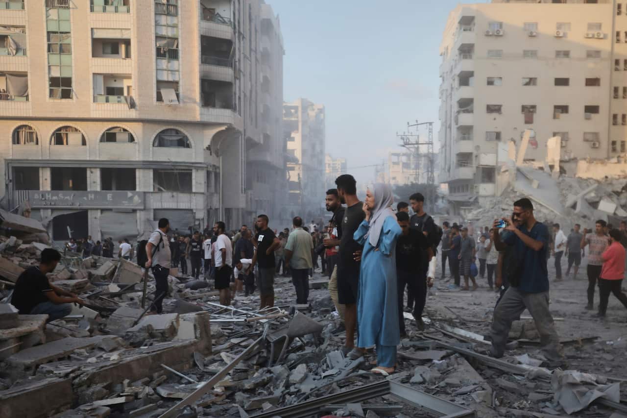A large group of Palestinian people standing amid the rubble of damaged buildings.