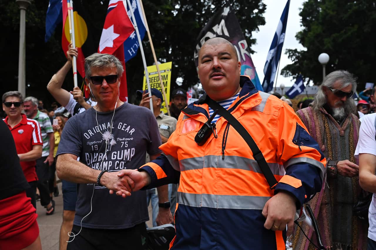 Two people shake hands as others walk behind at a rally.