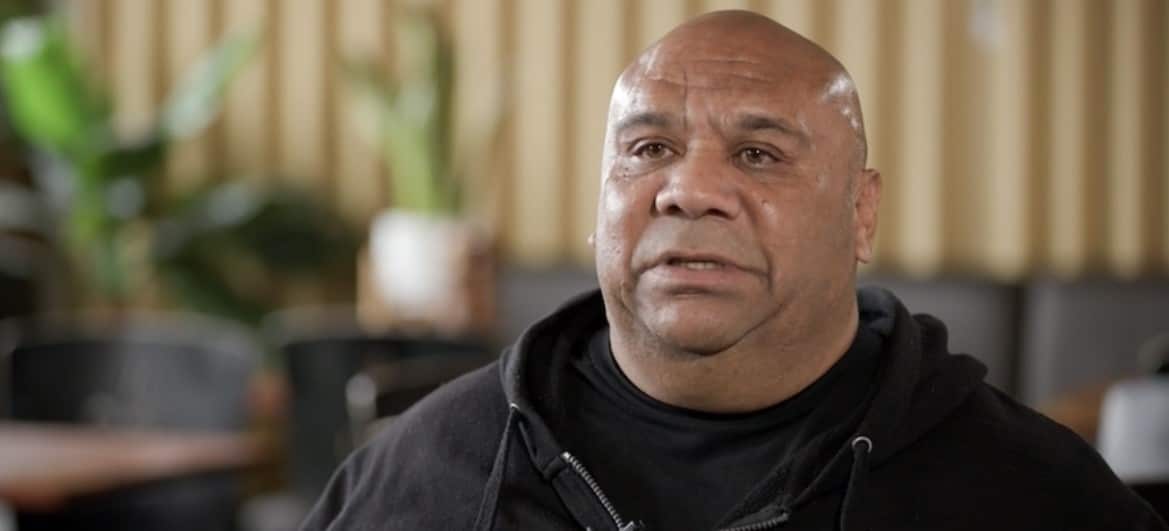 A man wearing a black t-shirt and jacket sitting inside 