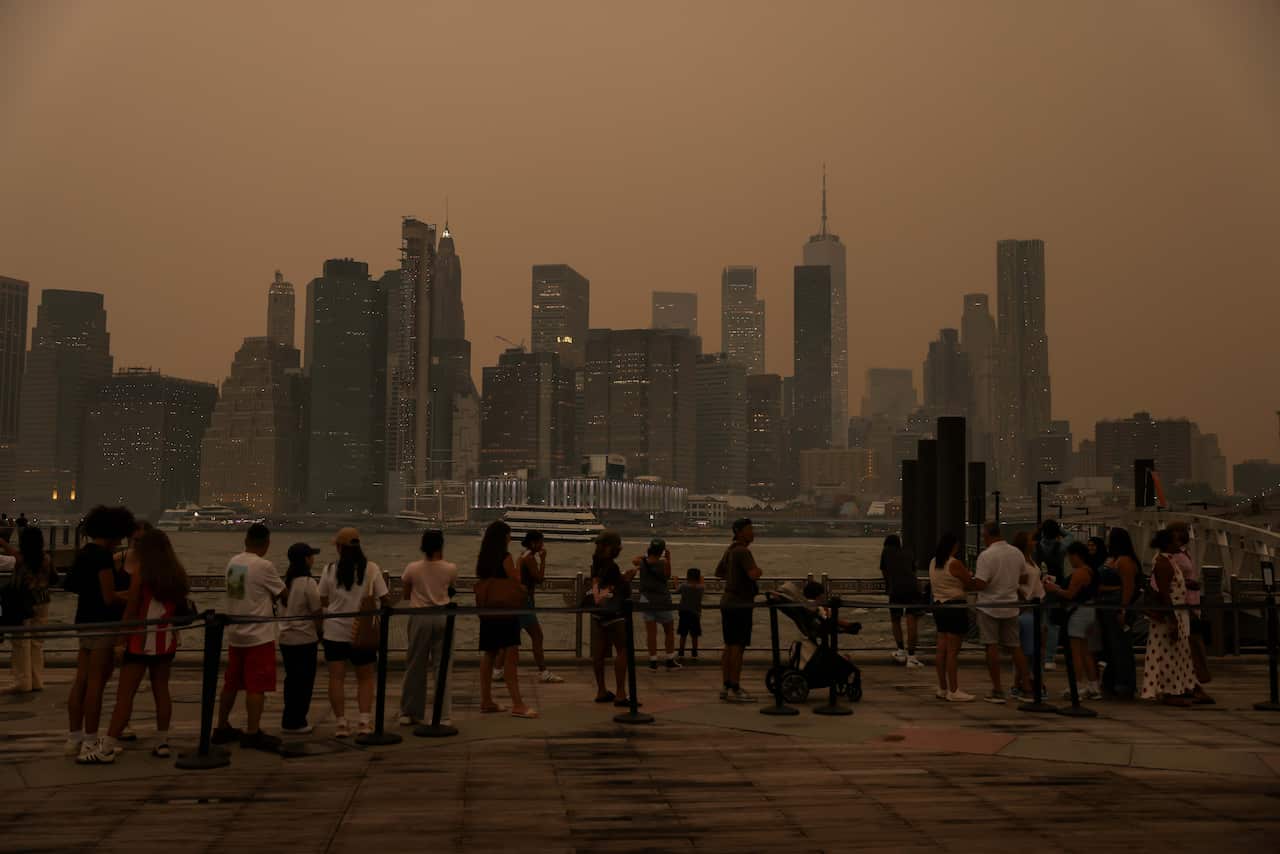 A group of people standing on a pier, with a skyline in the distance and hazy orange smoke.
