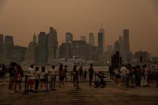 A group of people standing on a pier, with a skyline in the distance and hazy orange smoke.