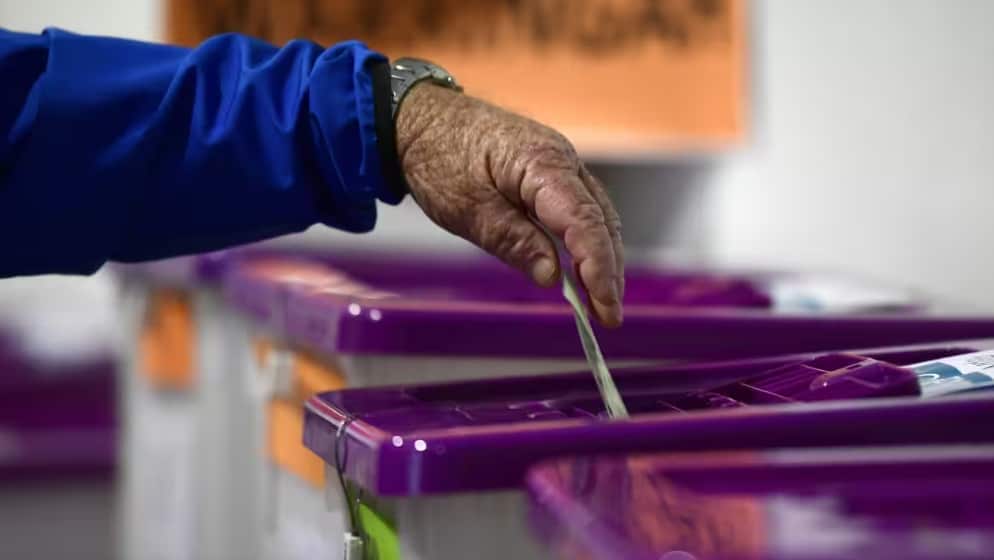 An elderly person is putting a vote in a ballot box.