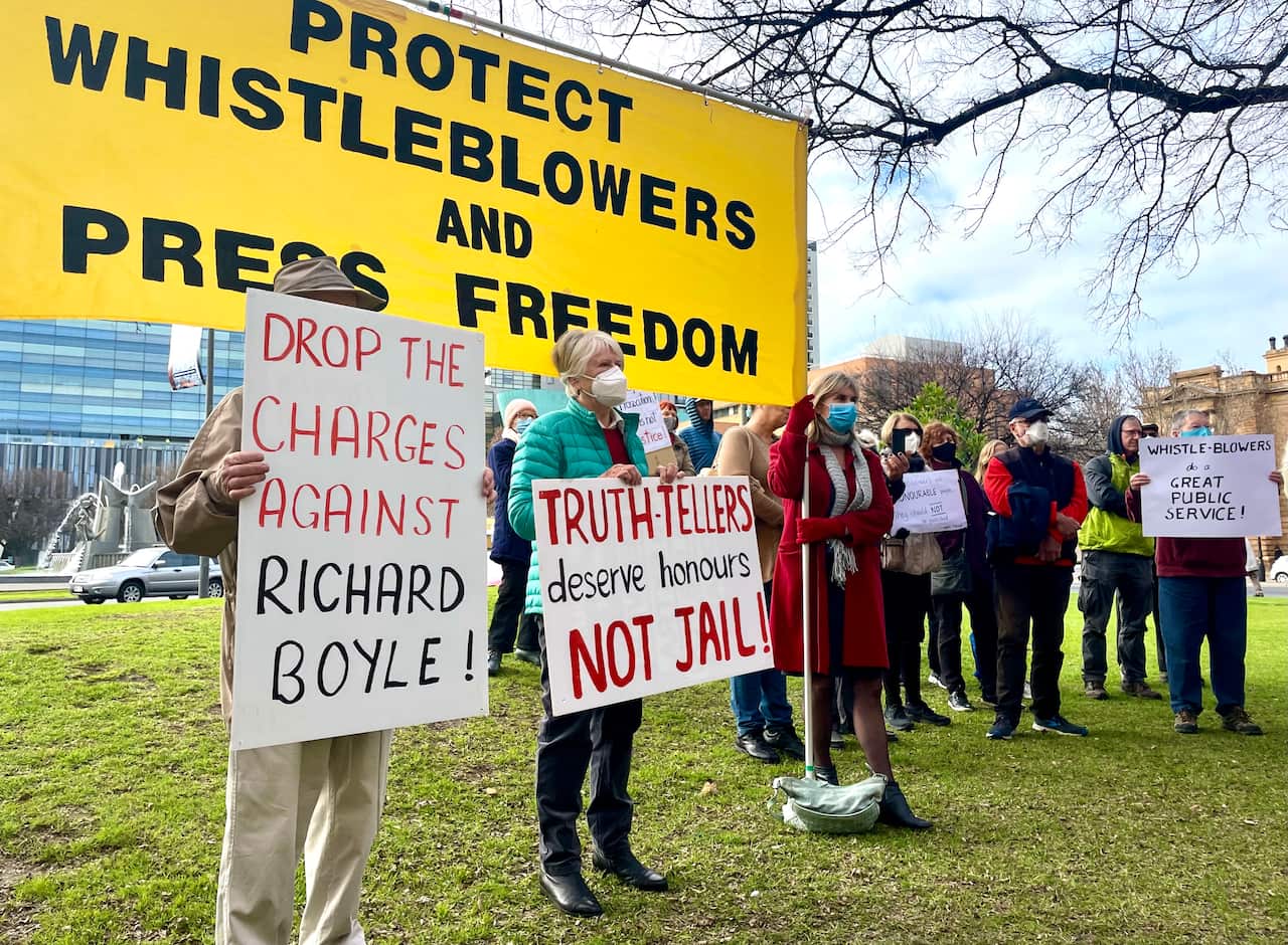People holding protest signs including one reading 'truth-tellers deserve honours not jail!'