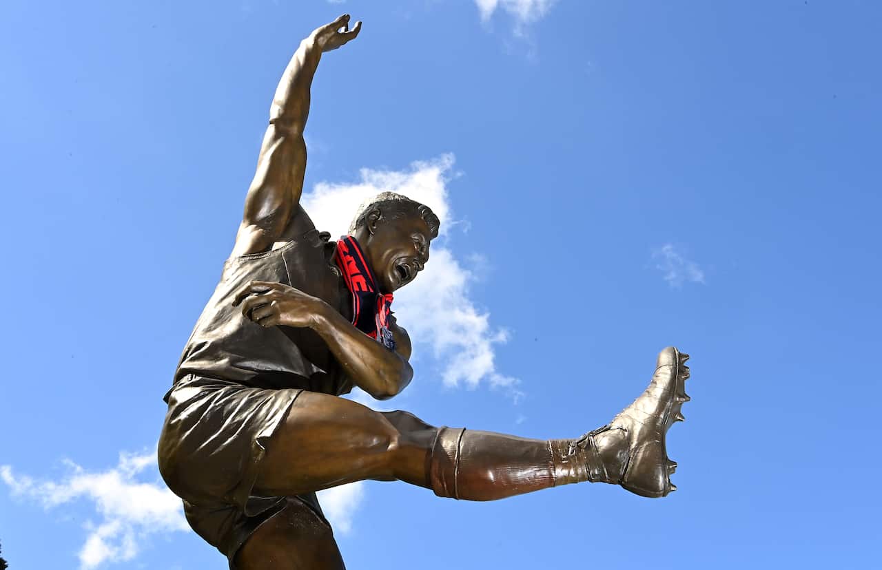 A bronze statue of a football player with a red and black scarf around its neck.