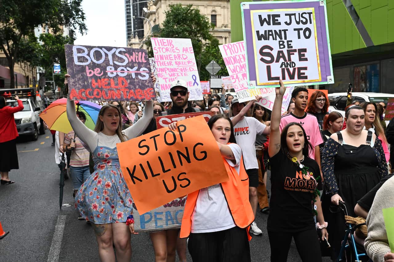 People march with signs during a protest, some reading "STOP KILLING US" and "WE JUST WANT TO BE SAFE AND LIVE".