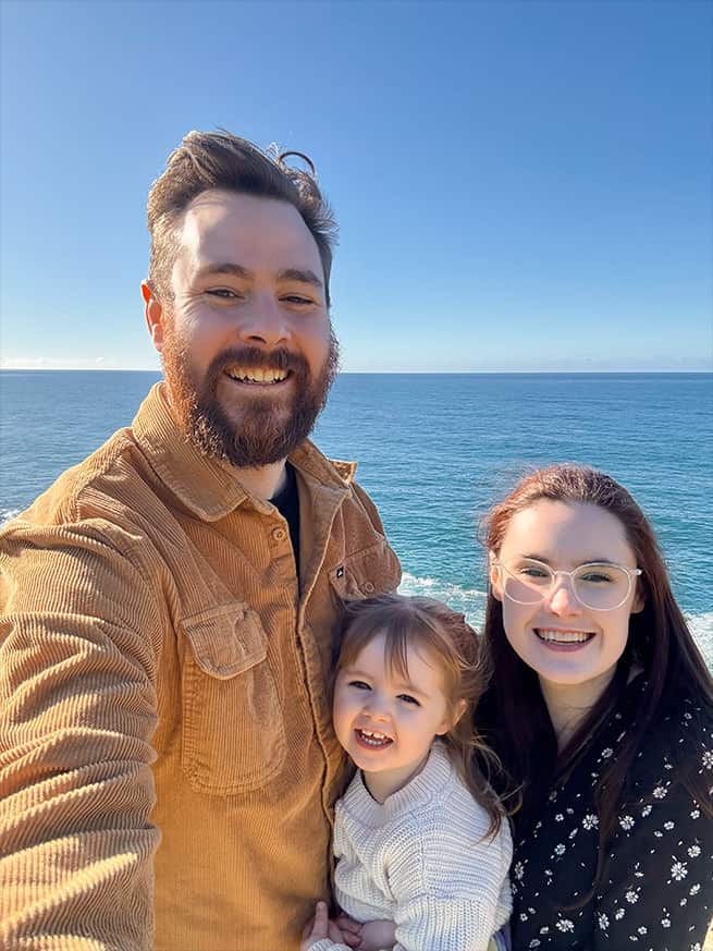 A young couple hold their small daughter. The sea is in the background.
