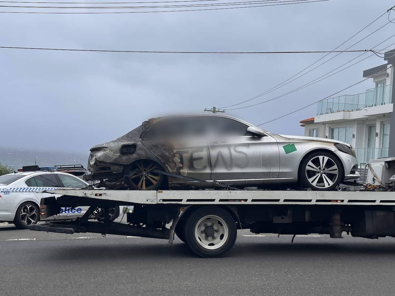 A burned out car with antisemitic graffiti is carried on a truck bed.