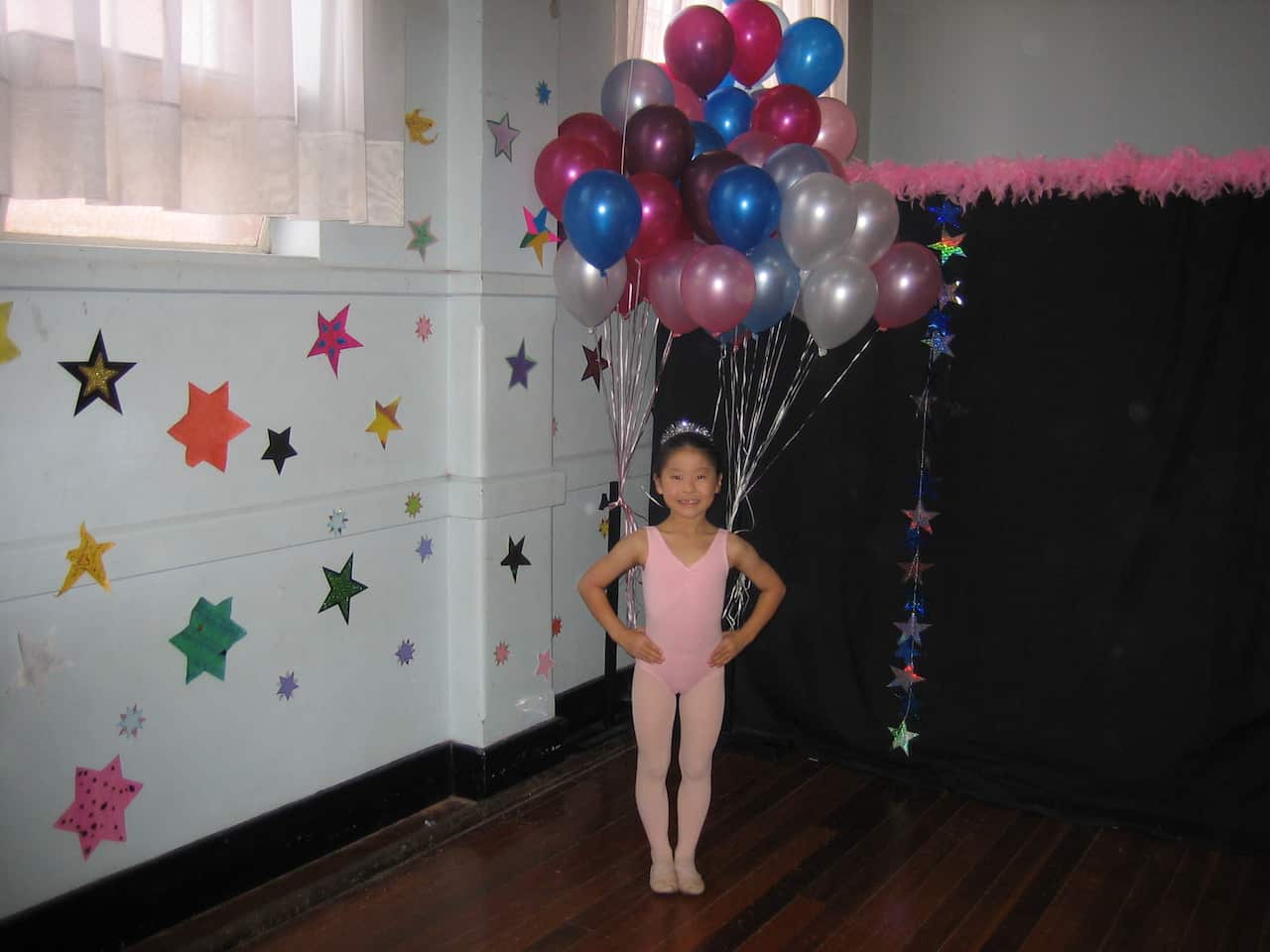 A young Chinese girl in a pink leotard with balloons on her back poses with her arms on her waist.