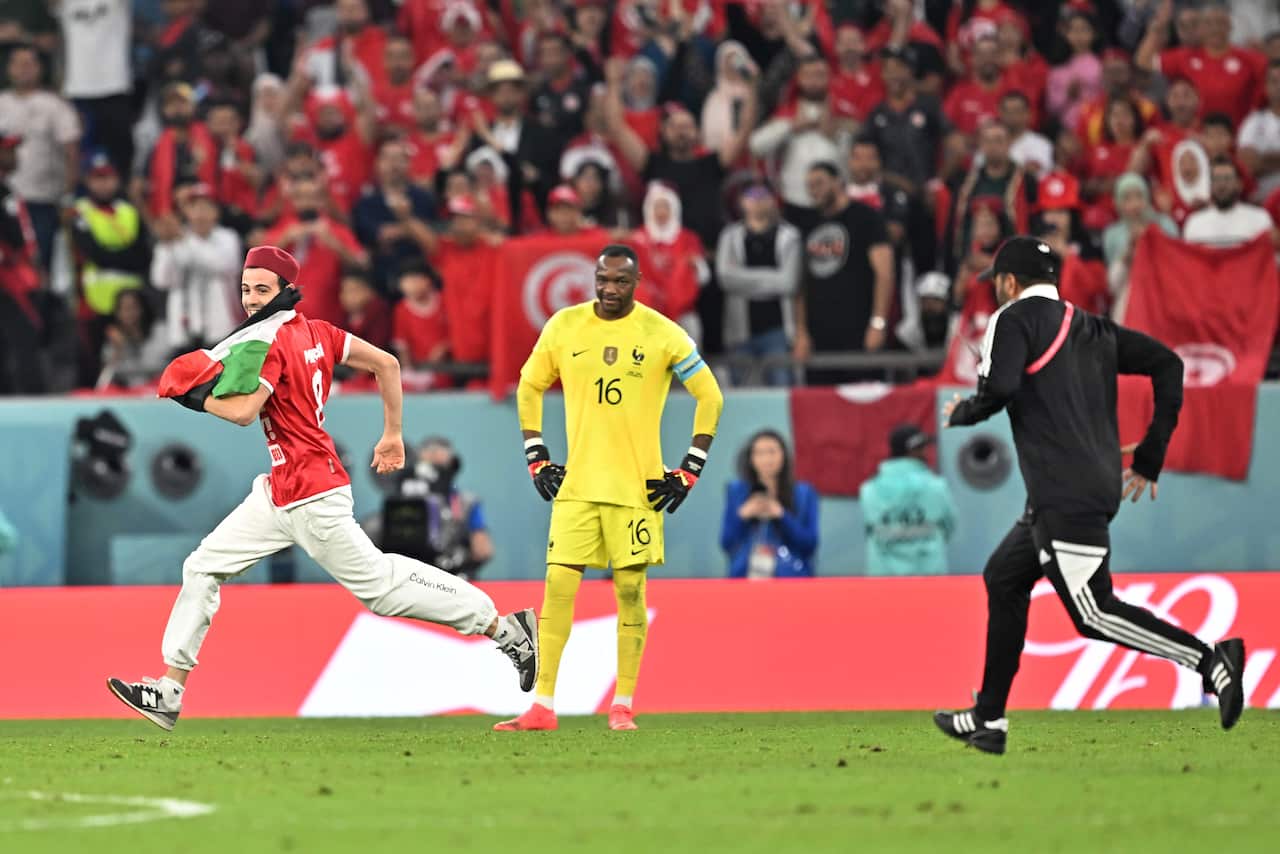 Man runs on field carrying Palestinian flag. Another man chases him down.