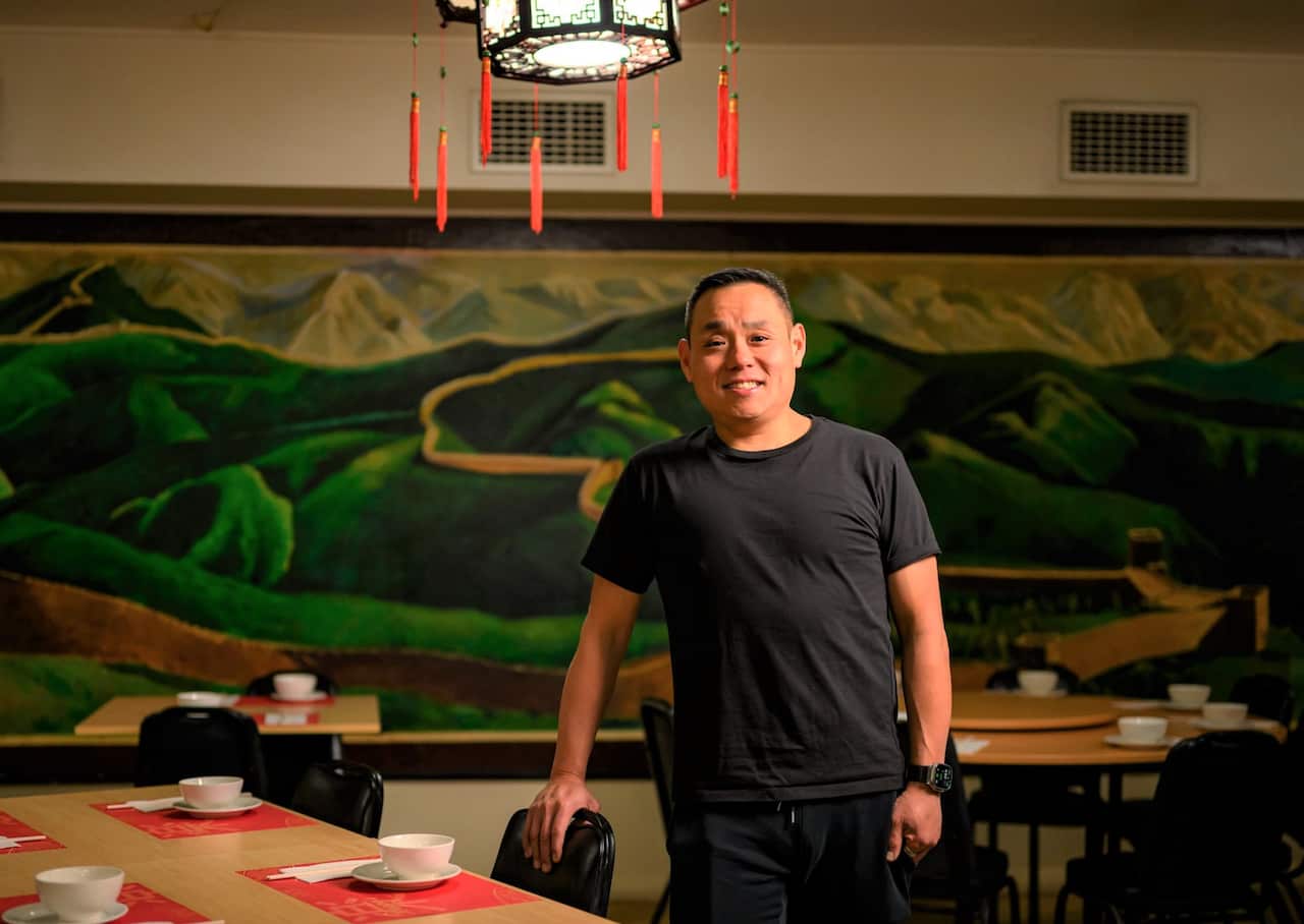 A man in a black round-neck t-shirt stands inside a fine-dining restaurant.