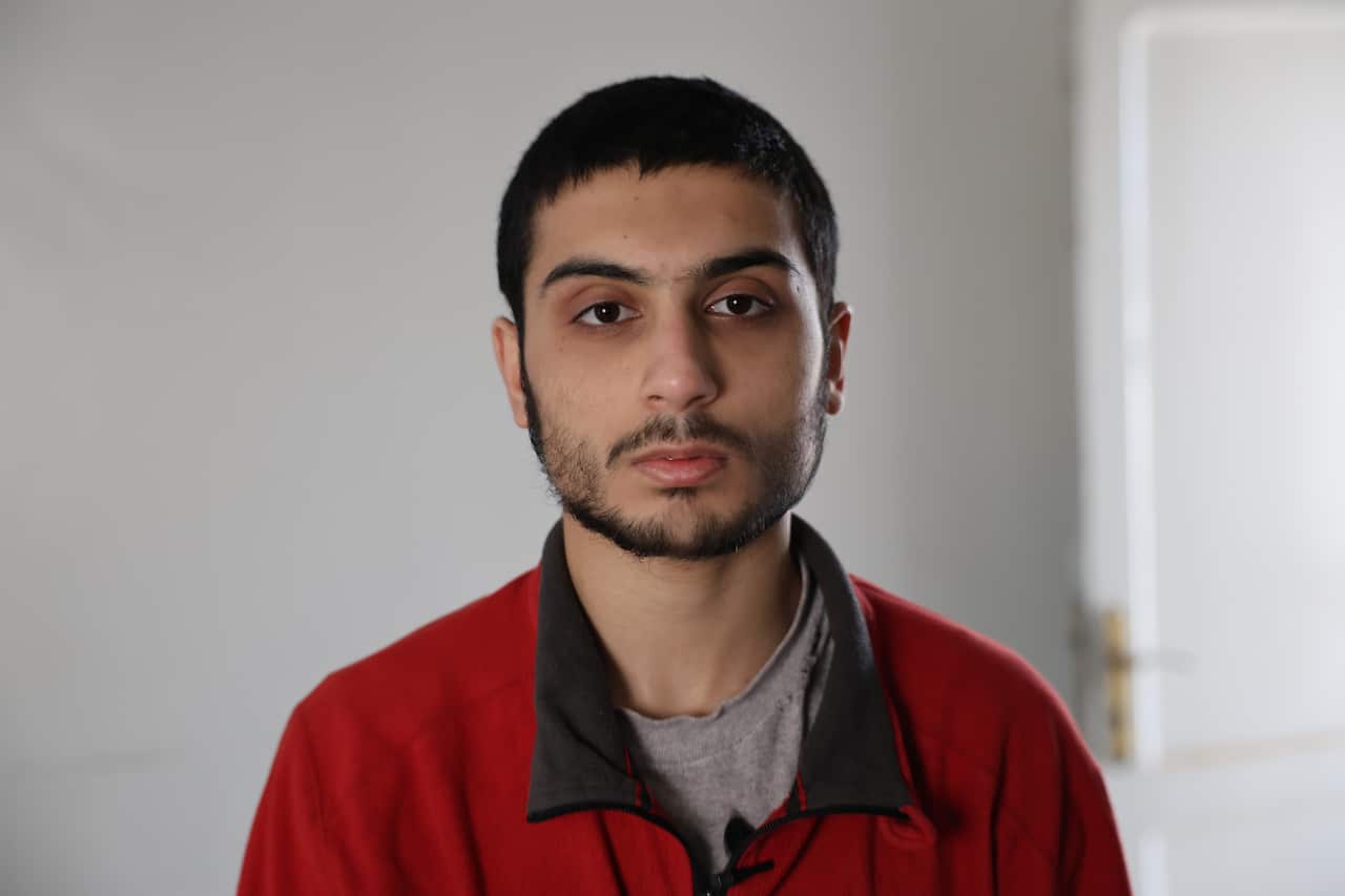 A head-and-shoulders shot of a young man in a red fleece looking at the camera with a serious expression.