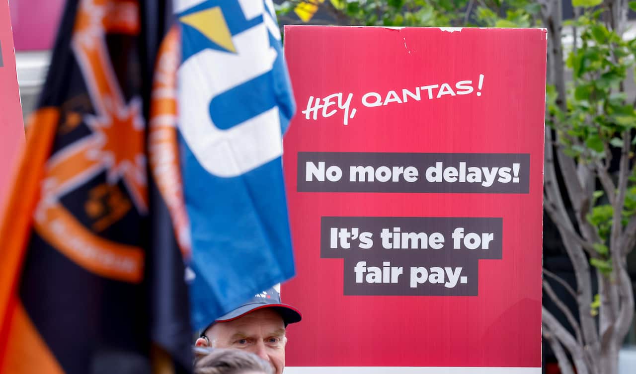 A red sign calling on Qantas to give workers a pay rise, with two union flags also visible.