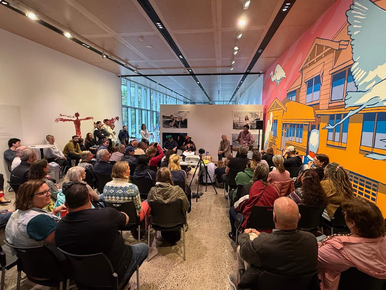 Rear view of a group of around 30 people are sitting in a narrow room.