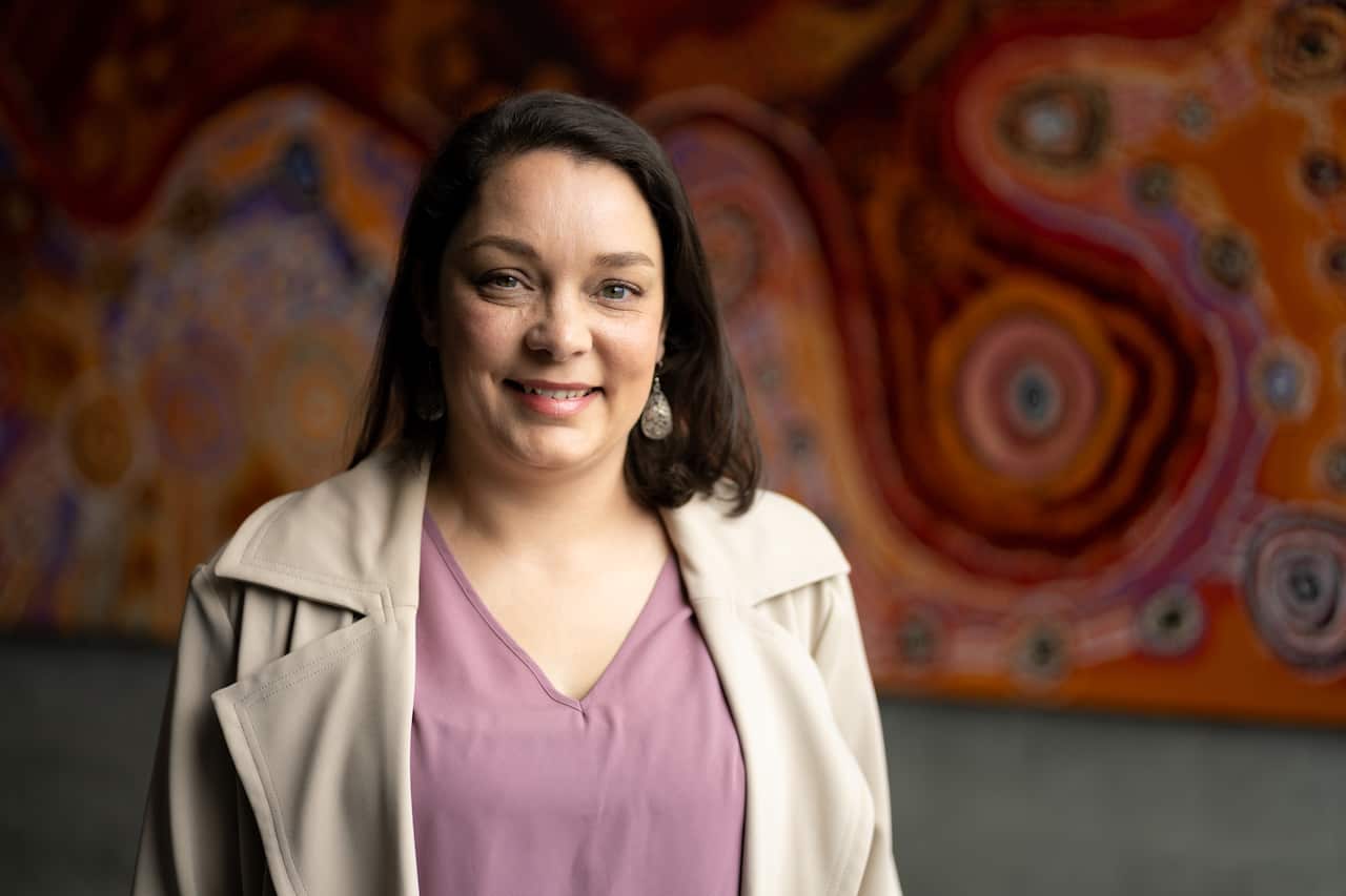 A woman in front of Indigenous artwork.