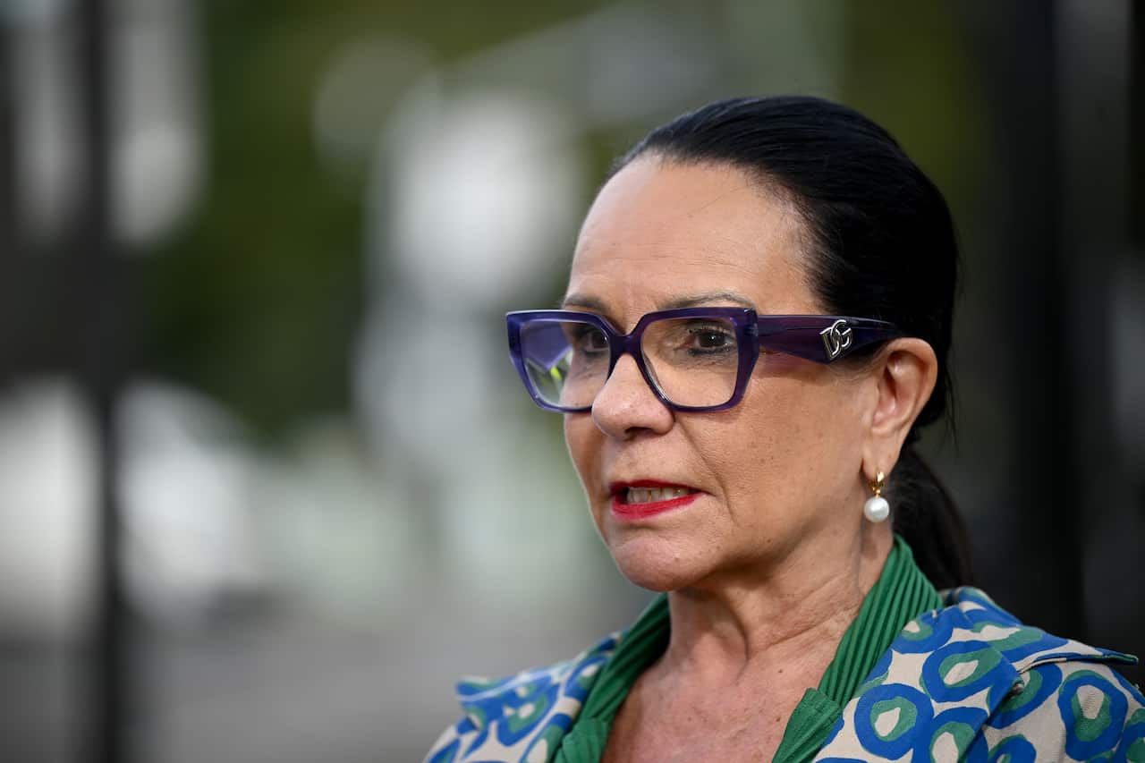 A woman with purple glasses and a printed-pattern top is speaking.