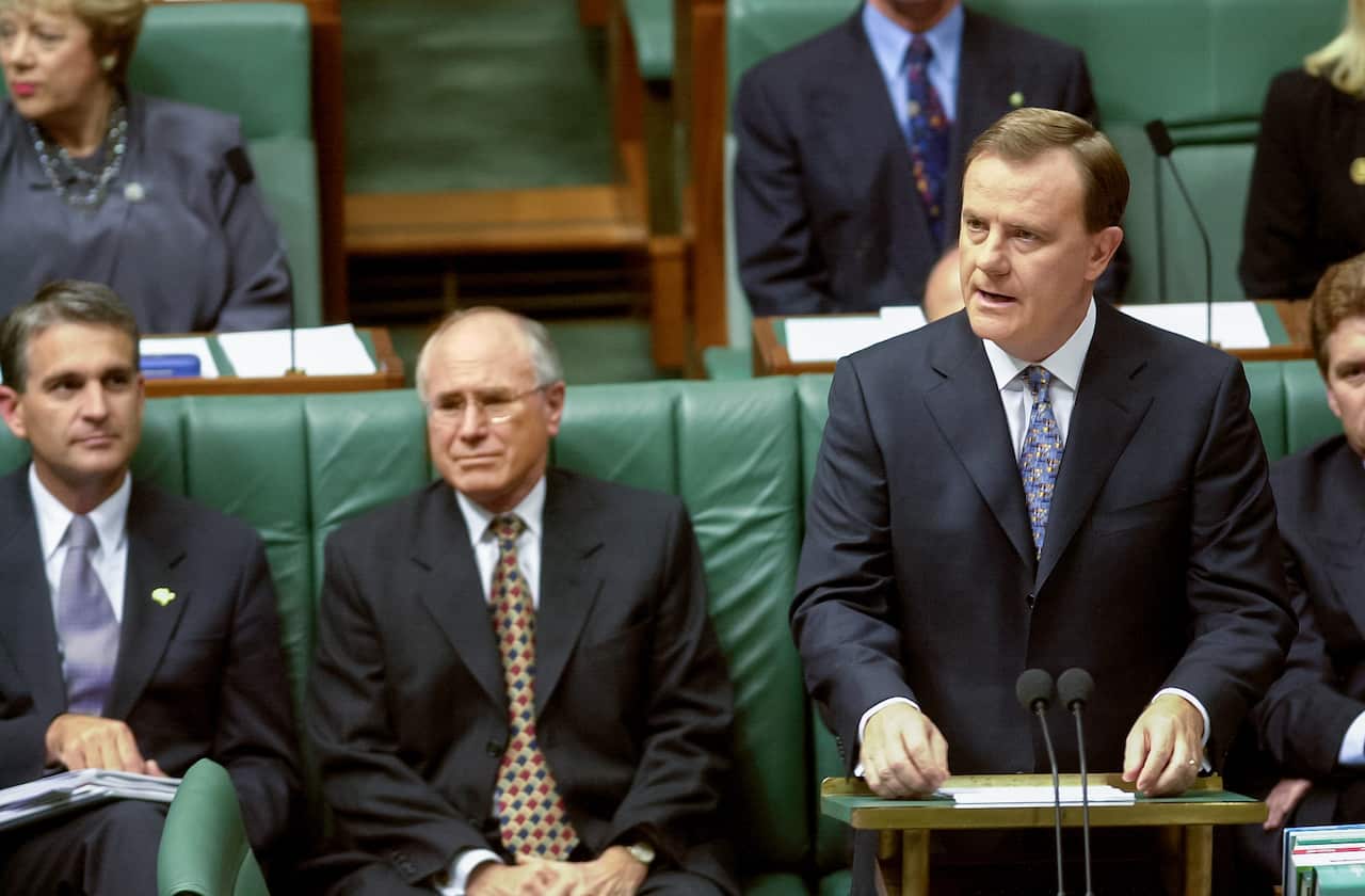 A man wearing a suit stands at a lectern inside the House of Representatives.