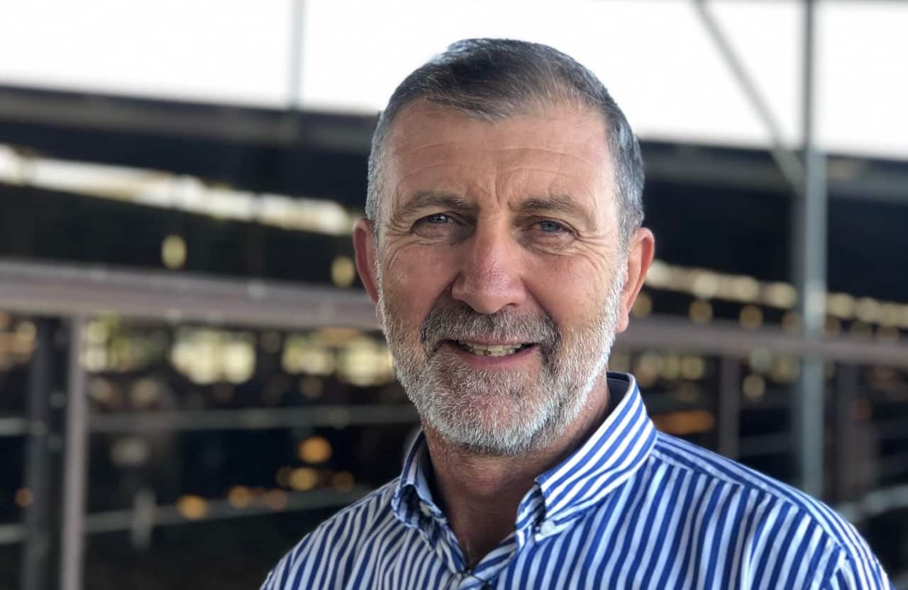 A man with grey hair wearing a blue and white striped shirt is smiling.
