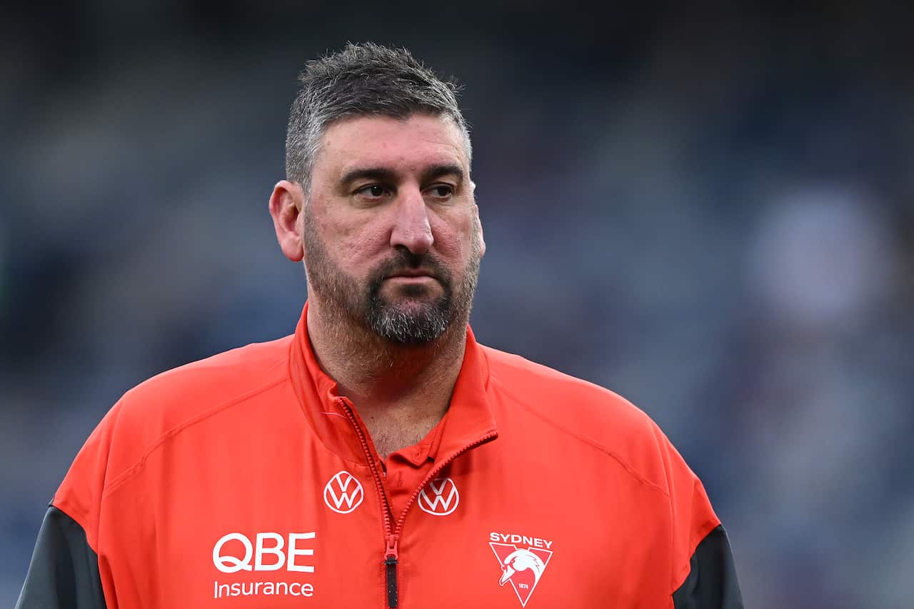 A middle-aged white man with short dark and grey hair and a beard, wearing a red Sydney Swans jacket