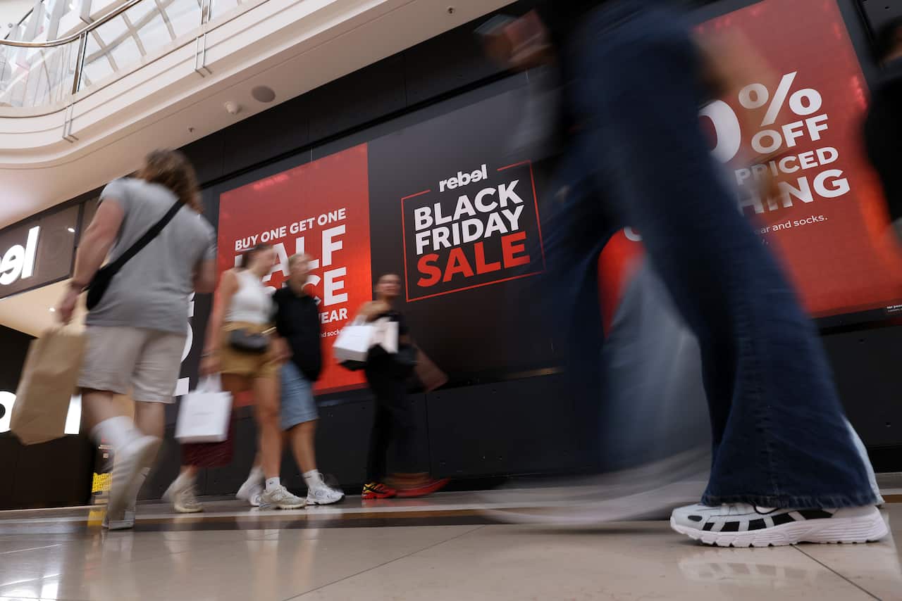Shoppers walk past a Rebel Sport 'Black Friday' shopping sign.